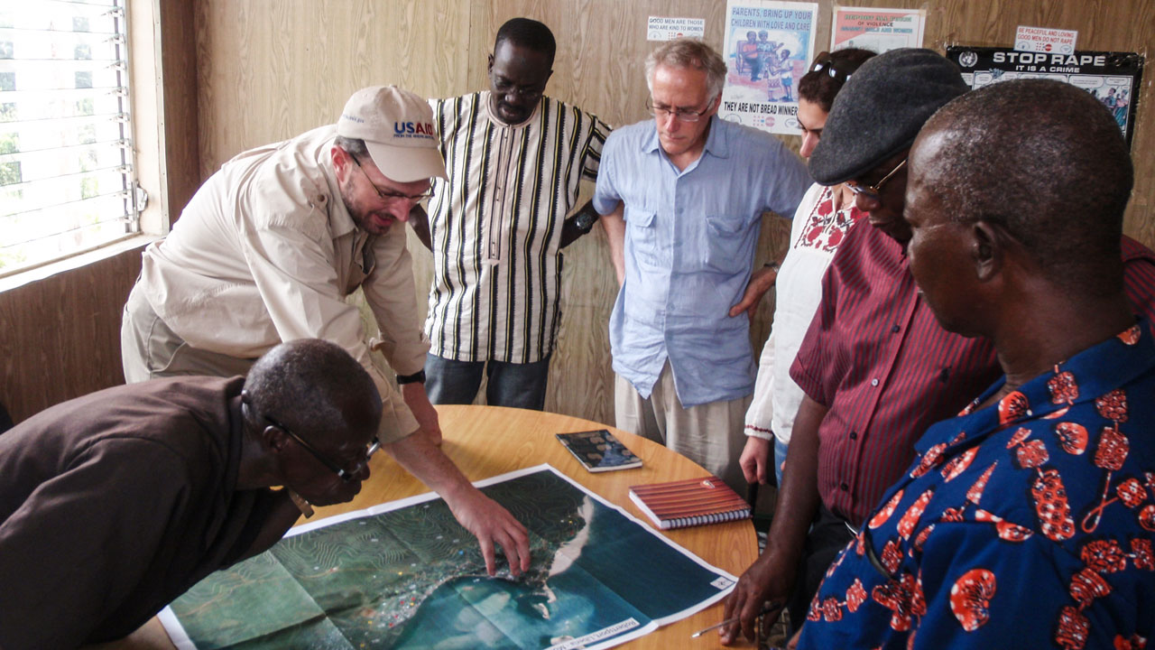 A group of men stand around a table looking at a map