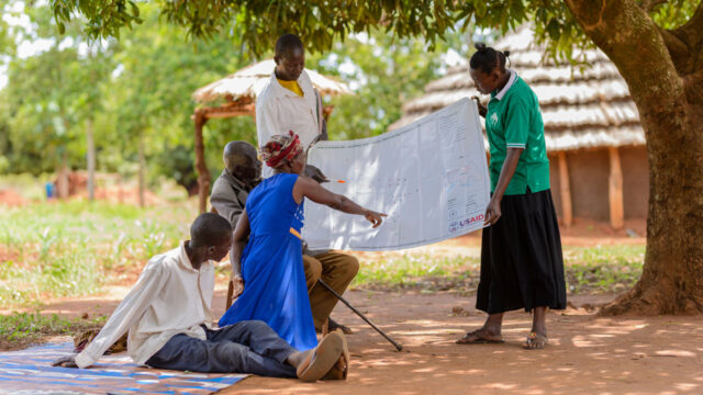Community members, some sitting some standing, look over village demarcations in Uganda
