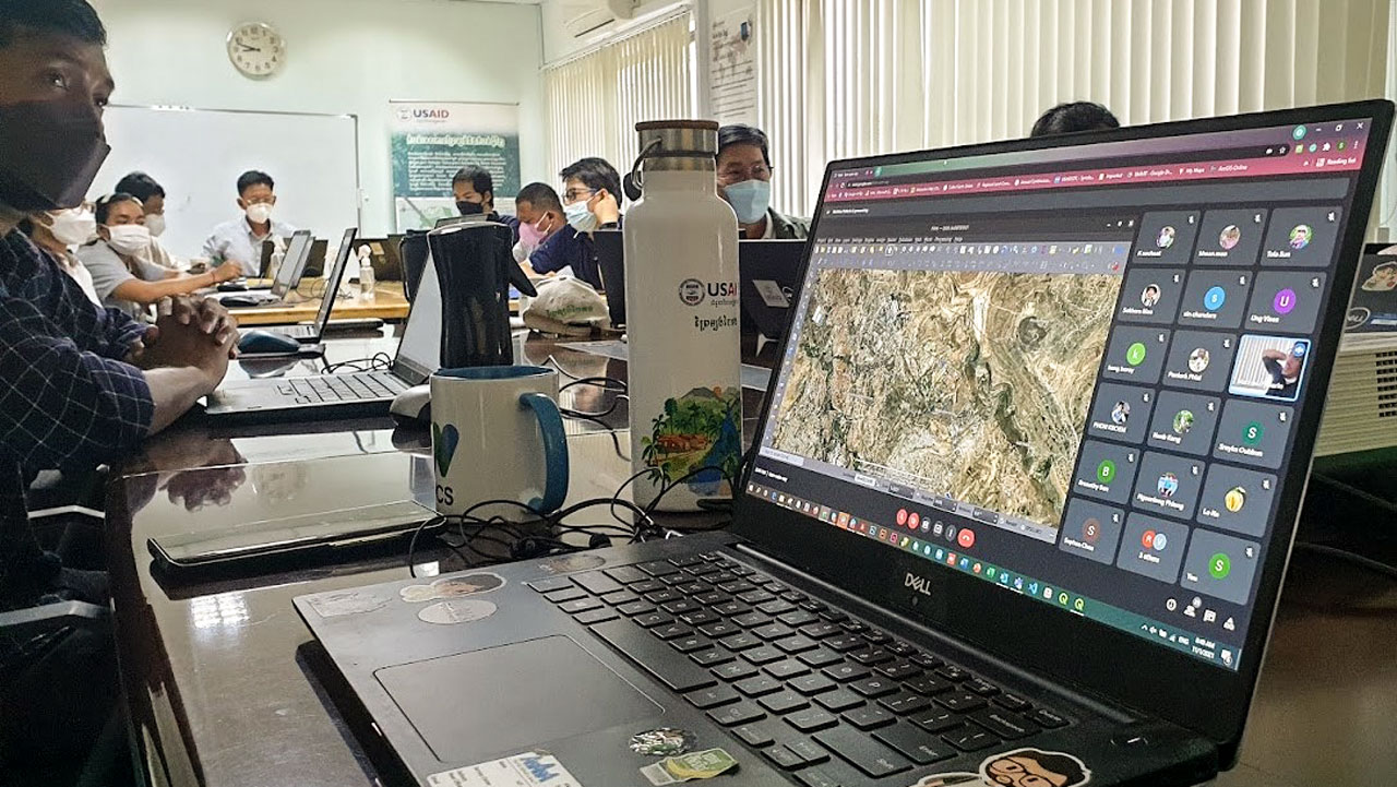 A closeup shot of a laptop showing a mapping program, with many other laptops and people in the background at a training