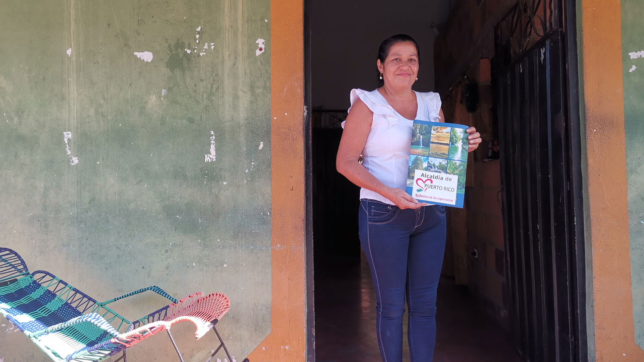 A woman in Colombia stands in a doorway holding her registered land certificate, supported by the Tetra Tech-led land rights program