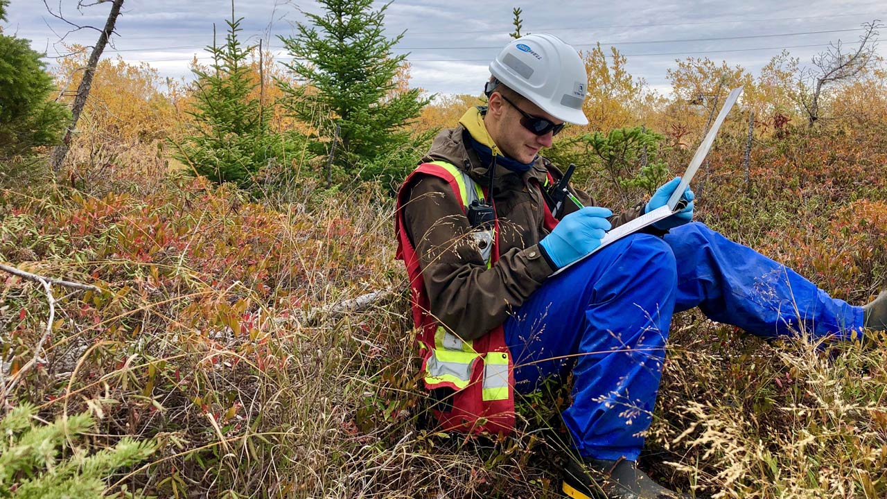 A Tetra Tech employee sits in a field recording information during permitting activities