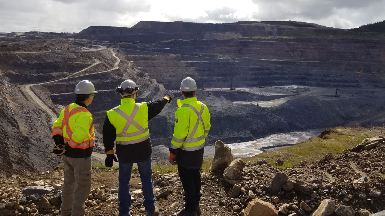 Three people in PPE look out over a mine