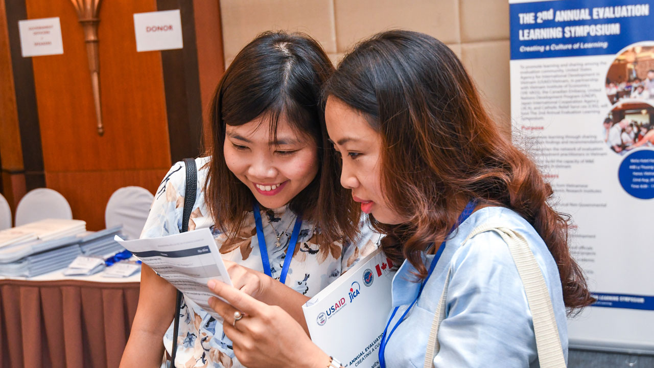 Two women stand close together looking at a piece of paper in Vietnam