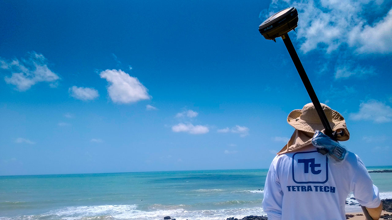 A Tetra Tech employee standing at Ponta Negra Beach holding equipment