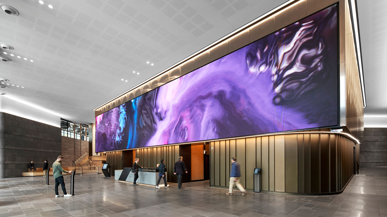 A huge, colorful screen displayed above the elevators in a large, busy office lobby