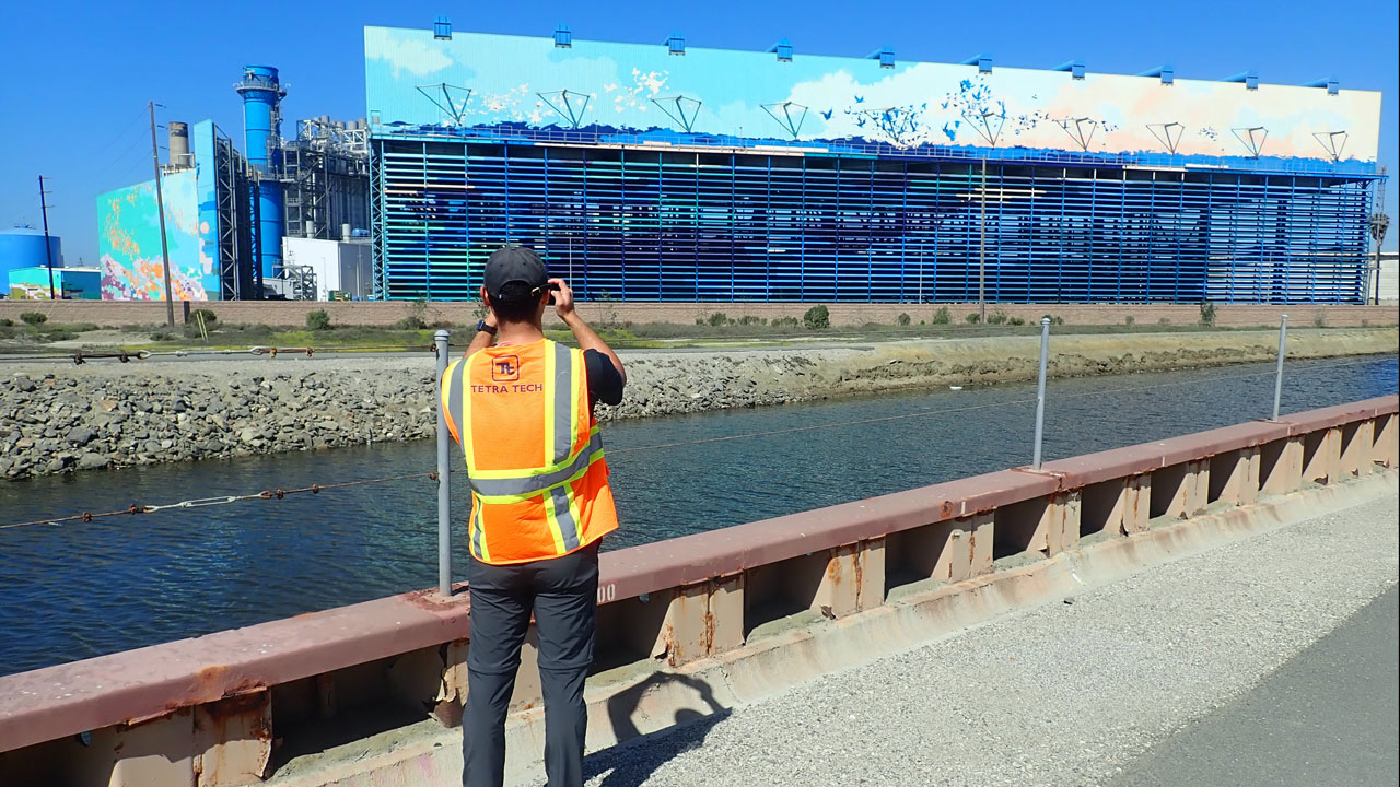 A Tetra Tech employee in a safety vest takes a photo of a water desalination plant during a channel inspection in California