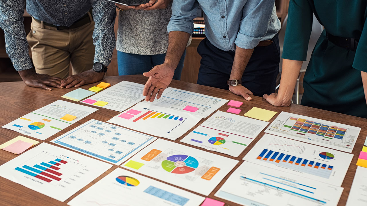 Four people standing around a table reviewing several graphs