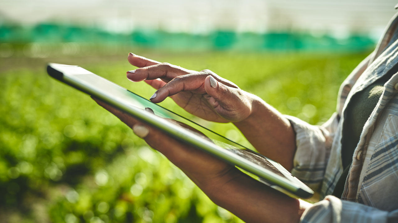 Shot of a woman's hand using a tablet in front of a farm