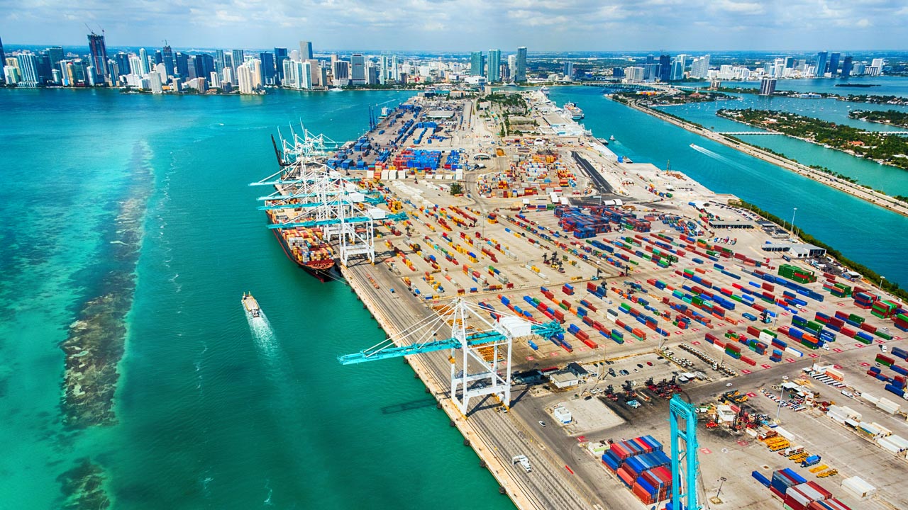 A wide-angle aerial view of the Port of Miami and Biscayne Bay, with the Miami skyline in the background