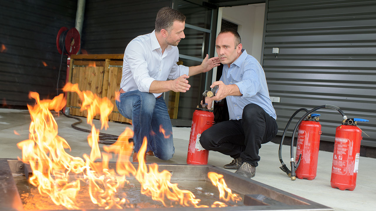 A trainer gives instructions to a student on how to extinguish a fire