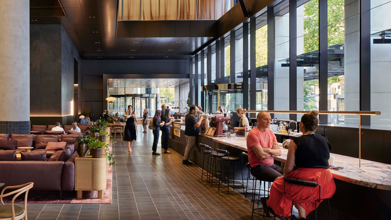 People sit in a café area with high ceilings, light and dark wall and ceiling treatments, and a mix of counter, table, and sofa seating