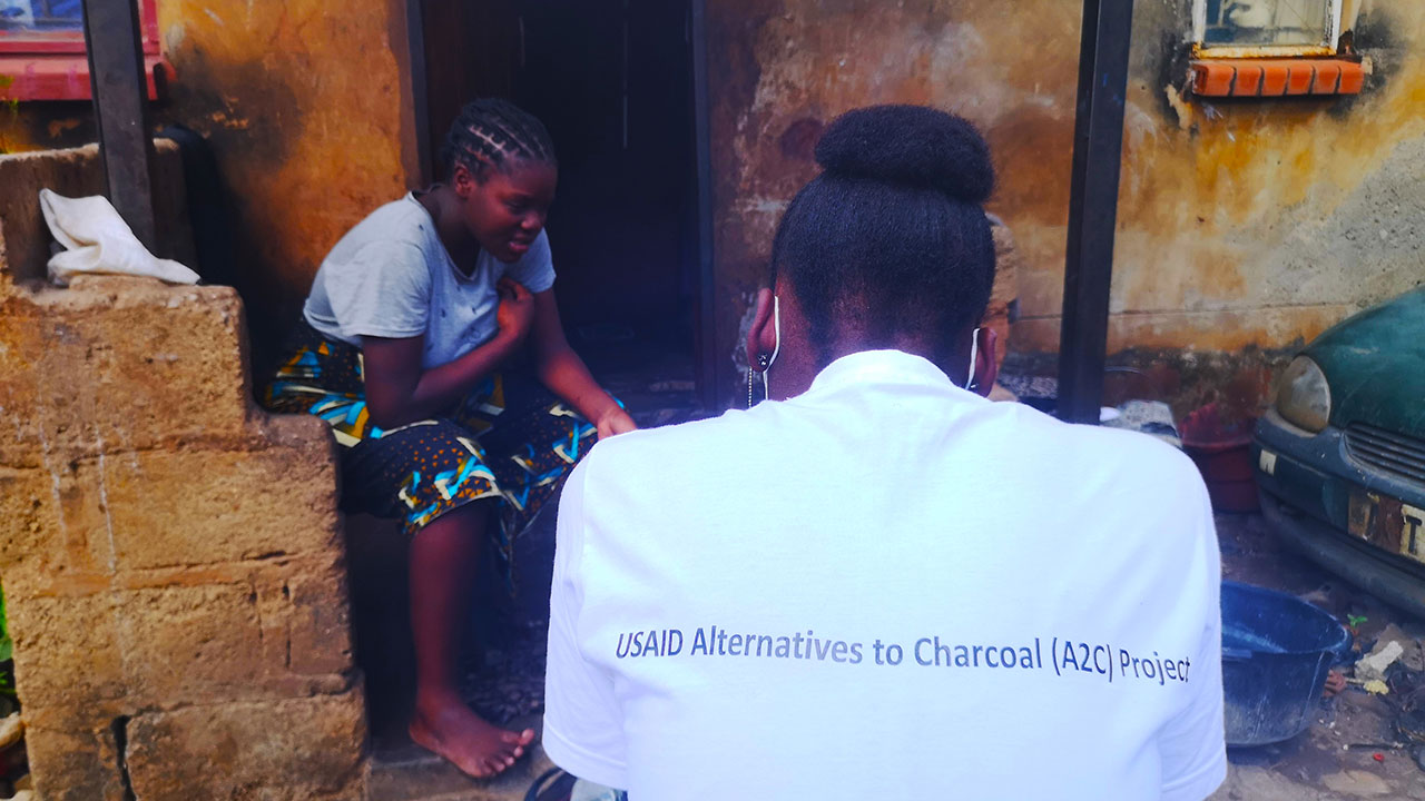 Two residents sit for interview on consumer preferences and knowledge; one wears a shirt that reads USAID Alternatives to Charcoal (A2C) Project