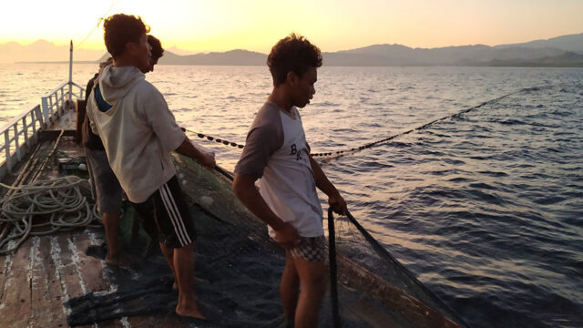 Three Indonesian fishermen cast a net while fishing offshore