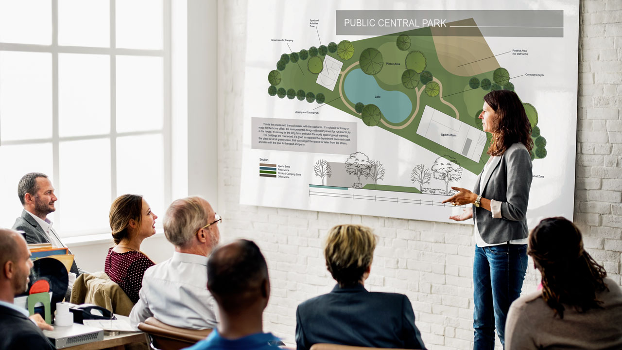 A classroom of people watching a speaker presenting with a large poster as campaign materials