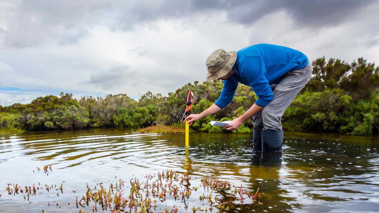 An employee standing in mid-calf high water takes measurements