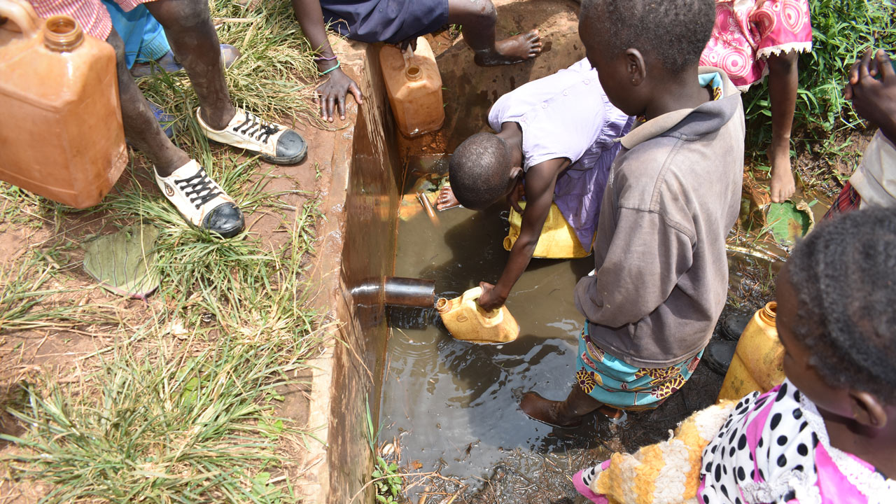Children in Uganda stand in a pool of water holding yellow water cans and gathering water from a faucet