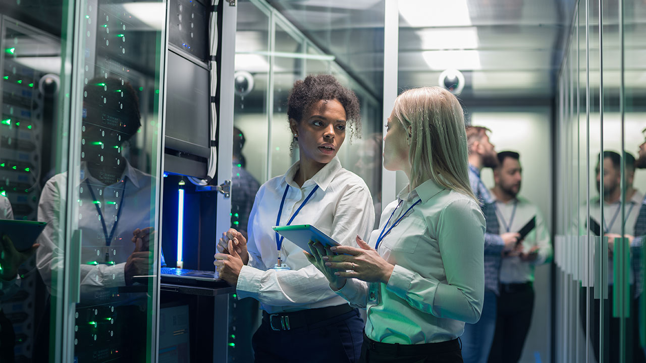 Two women speaking and accessing equipment in a large data center