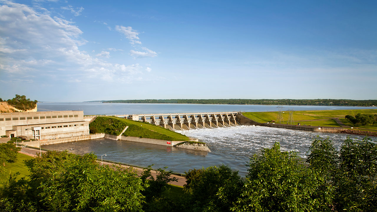 A dam with green landscape around it and a blue sky in the background
