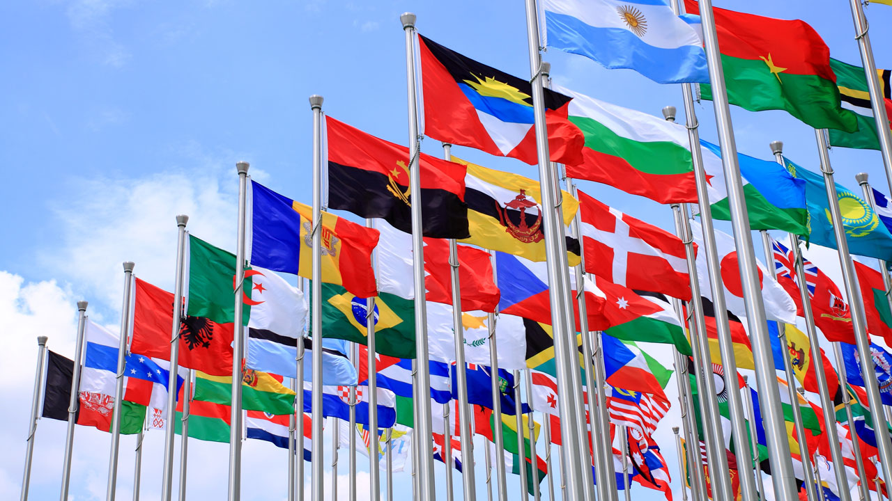 Flagpoles with flags of nations from around the world waving in the breeze under a blue sky