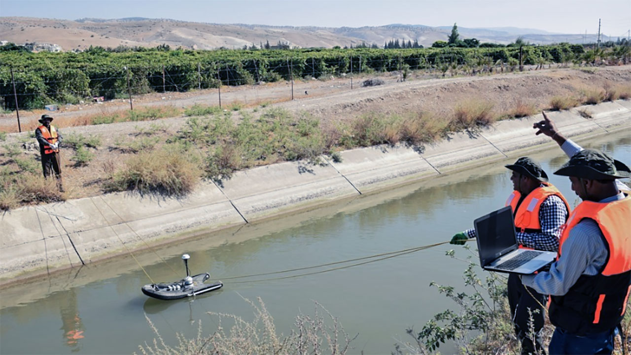 Two water flow engineers guide a measurement device down a narrow river in Jordan