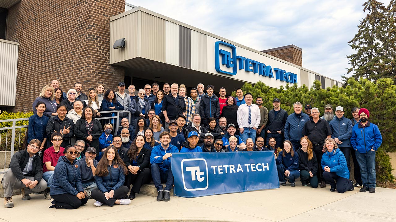 Large group of Tetra Tech employees in front of an office building holding Tetra Tech signage