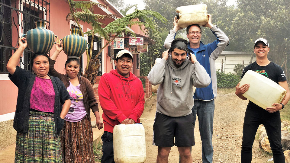 A group of people helping Mayan villagers in Guatemala carry water jugs to their homes