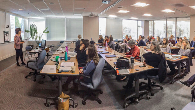 A side-view of a classroom filled with people listening attentively to a presenter