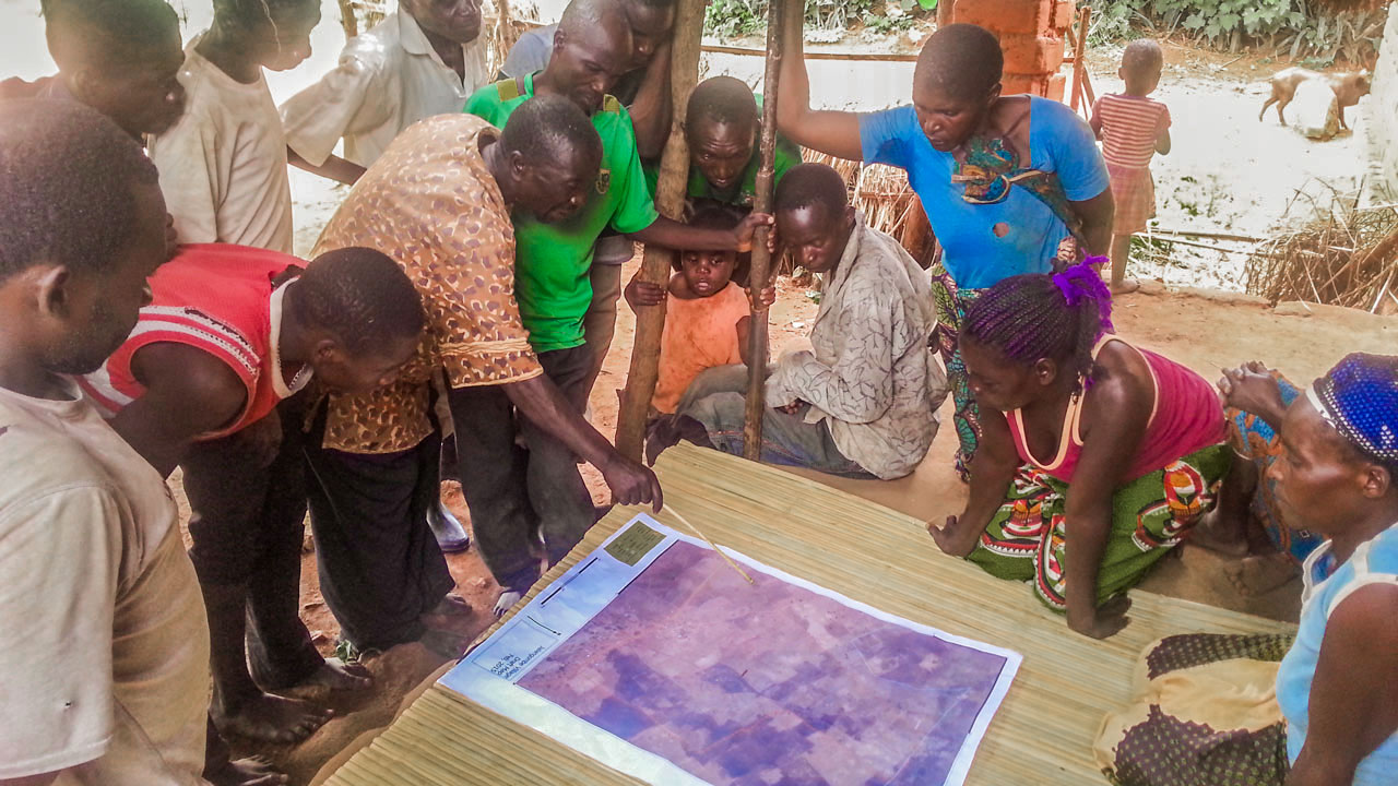 A group of people standing around a table, pointing at a map, and discussing property rights