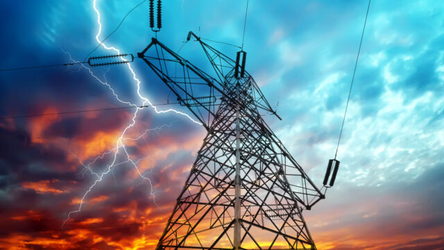 A transmission tower and power lines with lightning against a dramatic sky at sunset