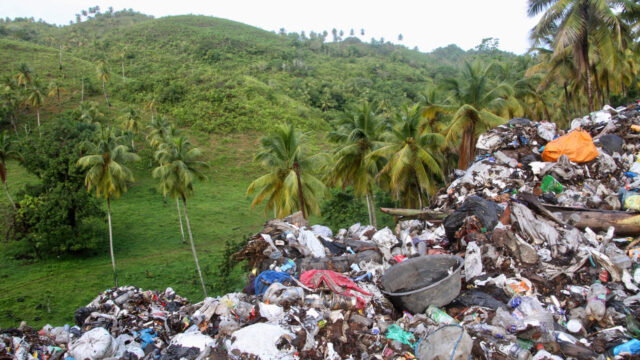 Open dump site with large pile of waste and plastic pollution next to an ecologically significant landscape