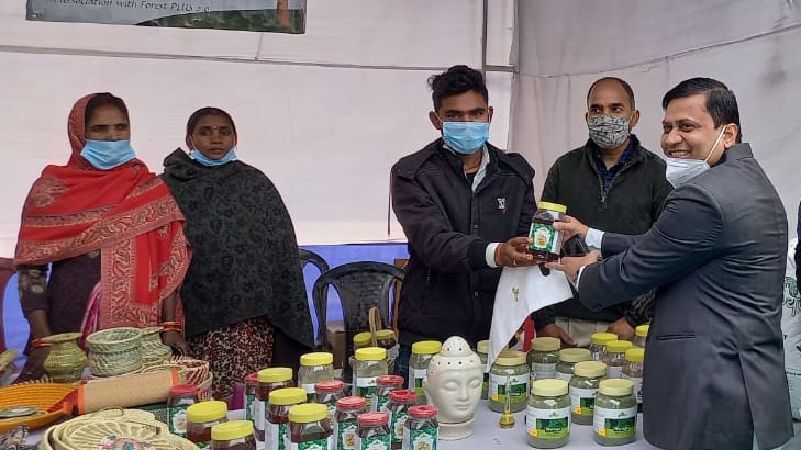 A group of people standing next to a table with jars as part of a Moringa leaf value chain set up by Tetra Tech’s Forest-PLUS 2.0