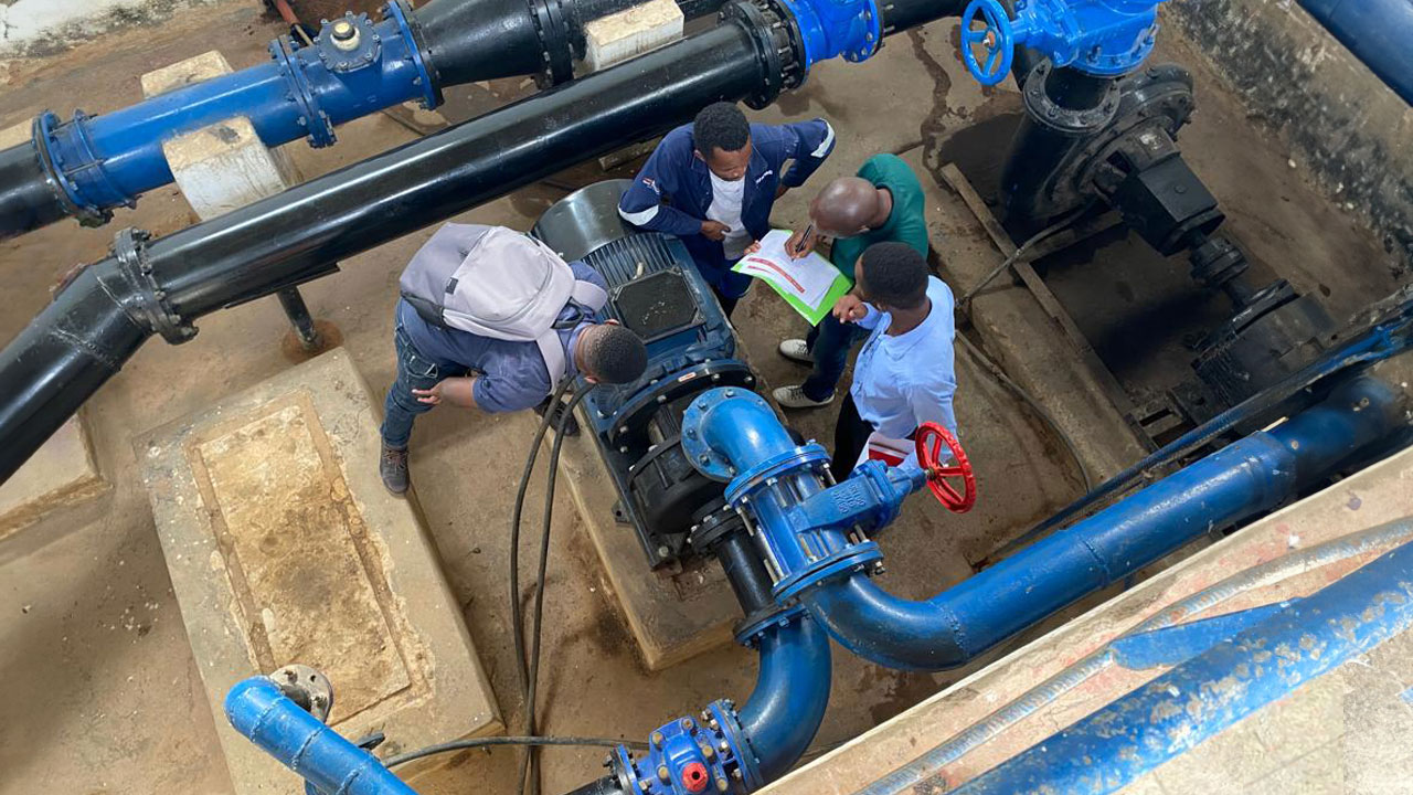 A small group of men compares a manual with the water pipes and system in front of them