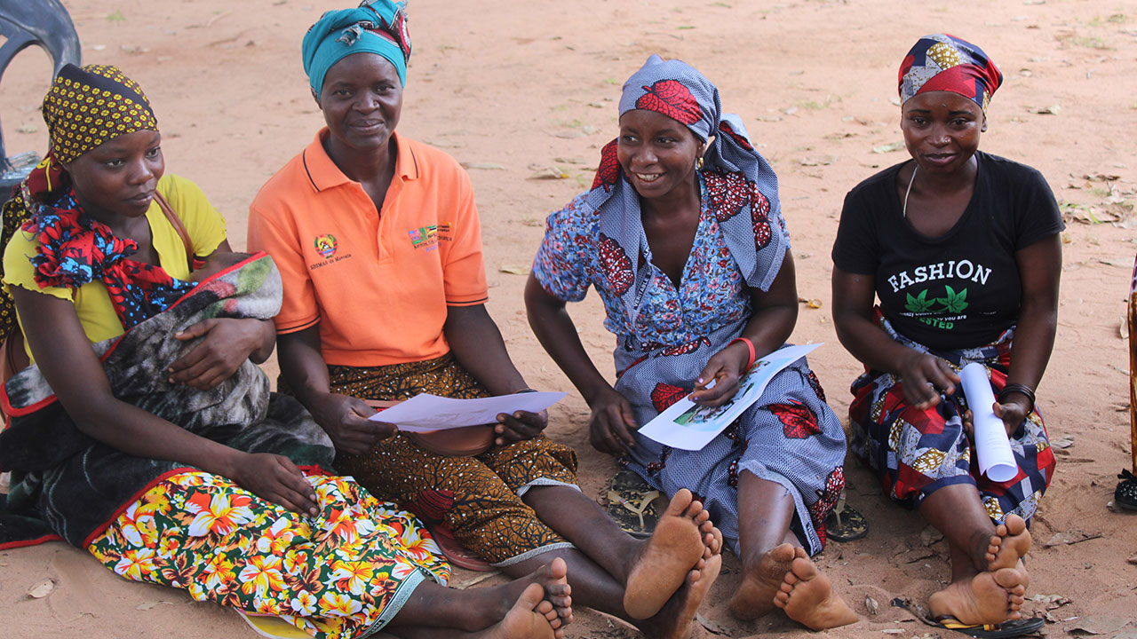 Four women sit on the ground and discuss training information during a workshop