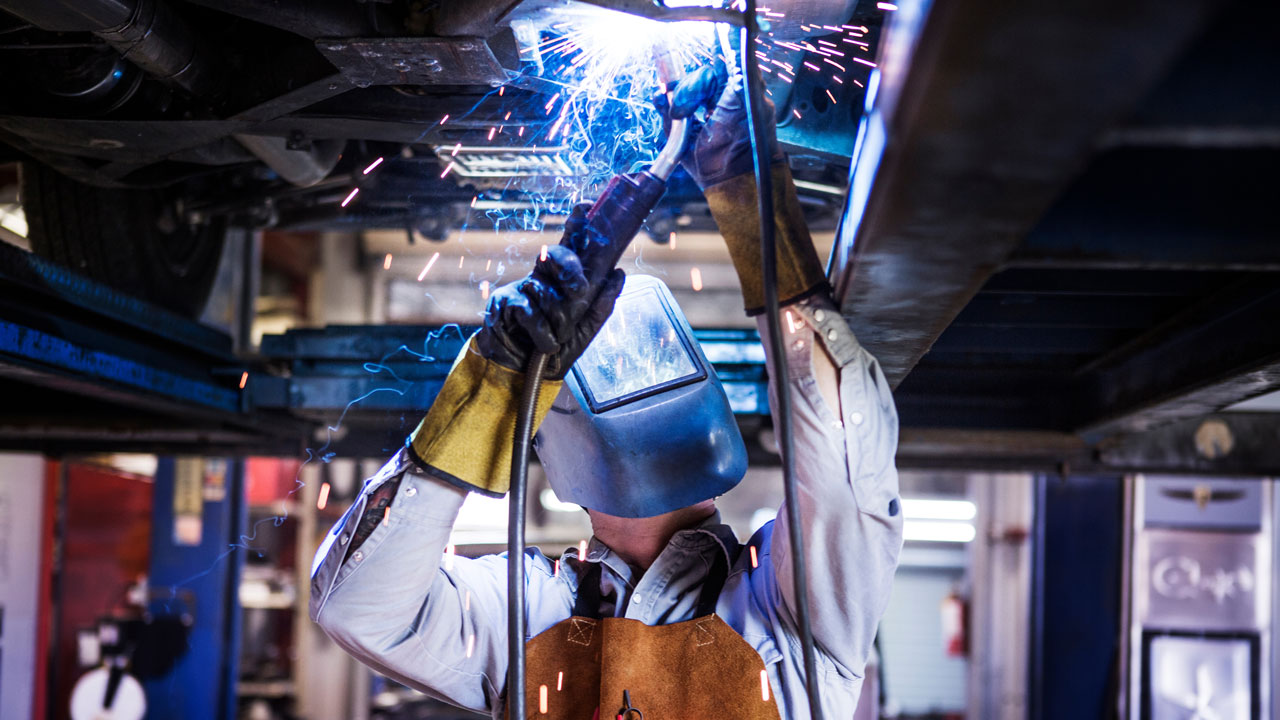 Welder in protective equipment welding a joint underneath a car chassis