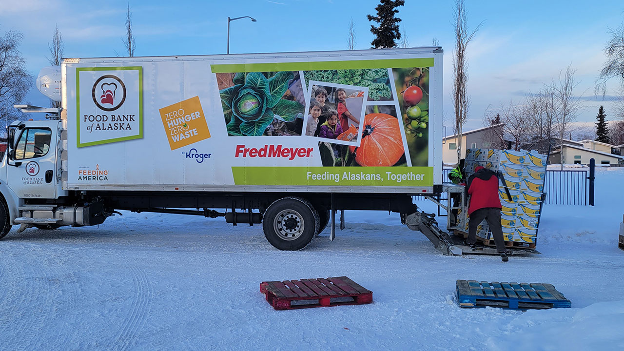 Two workers unload food boxes from a food bank truck