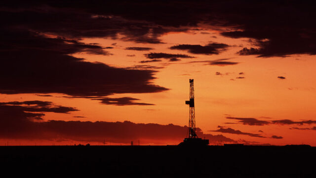 Silhouetted rig stands against a vibrant orange and purple sunset, with dramatic clouds in the sky