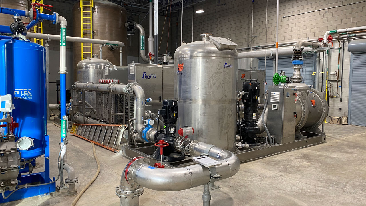 A large industrial setup featuring multiple metallic tanks, piping systems, and electrical components in a spacious facility