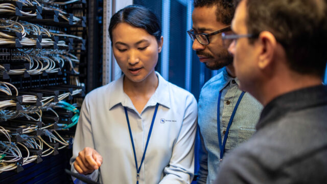 Three IT professionals discussing and examining network cables inside a server room