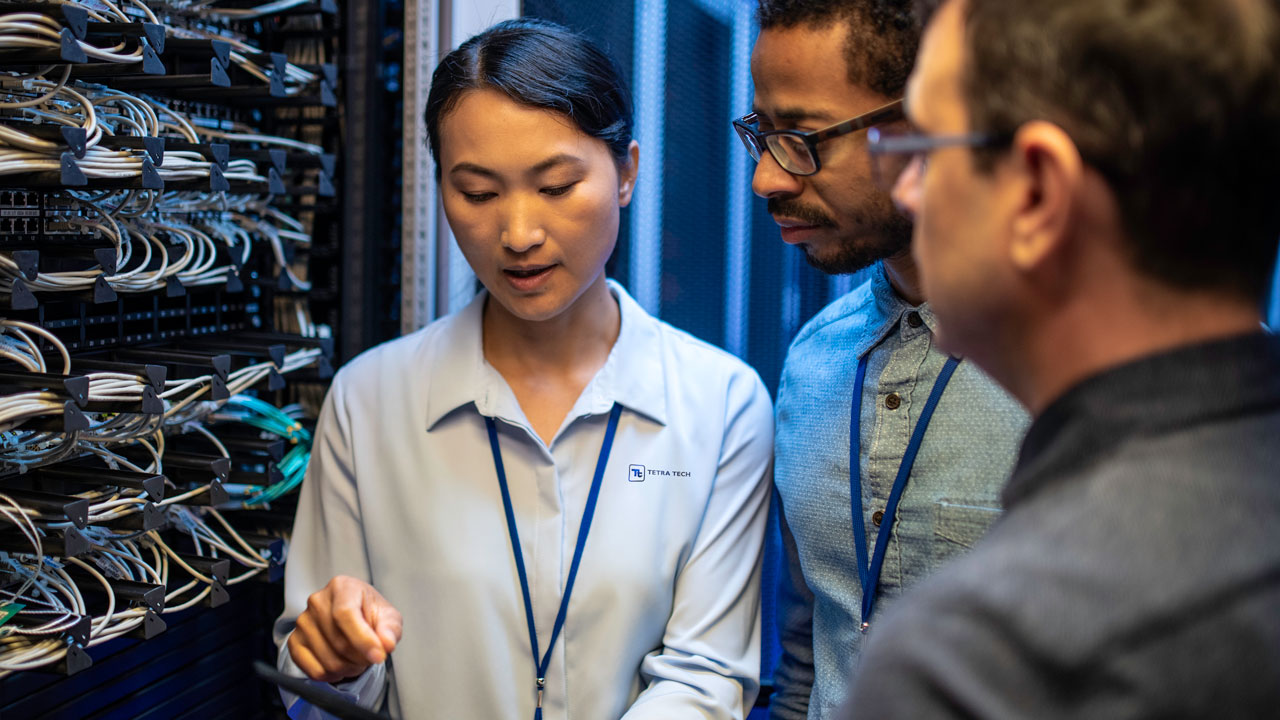 Three IT professionals discussing and examining network cables inside a server room