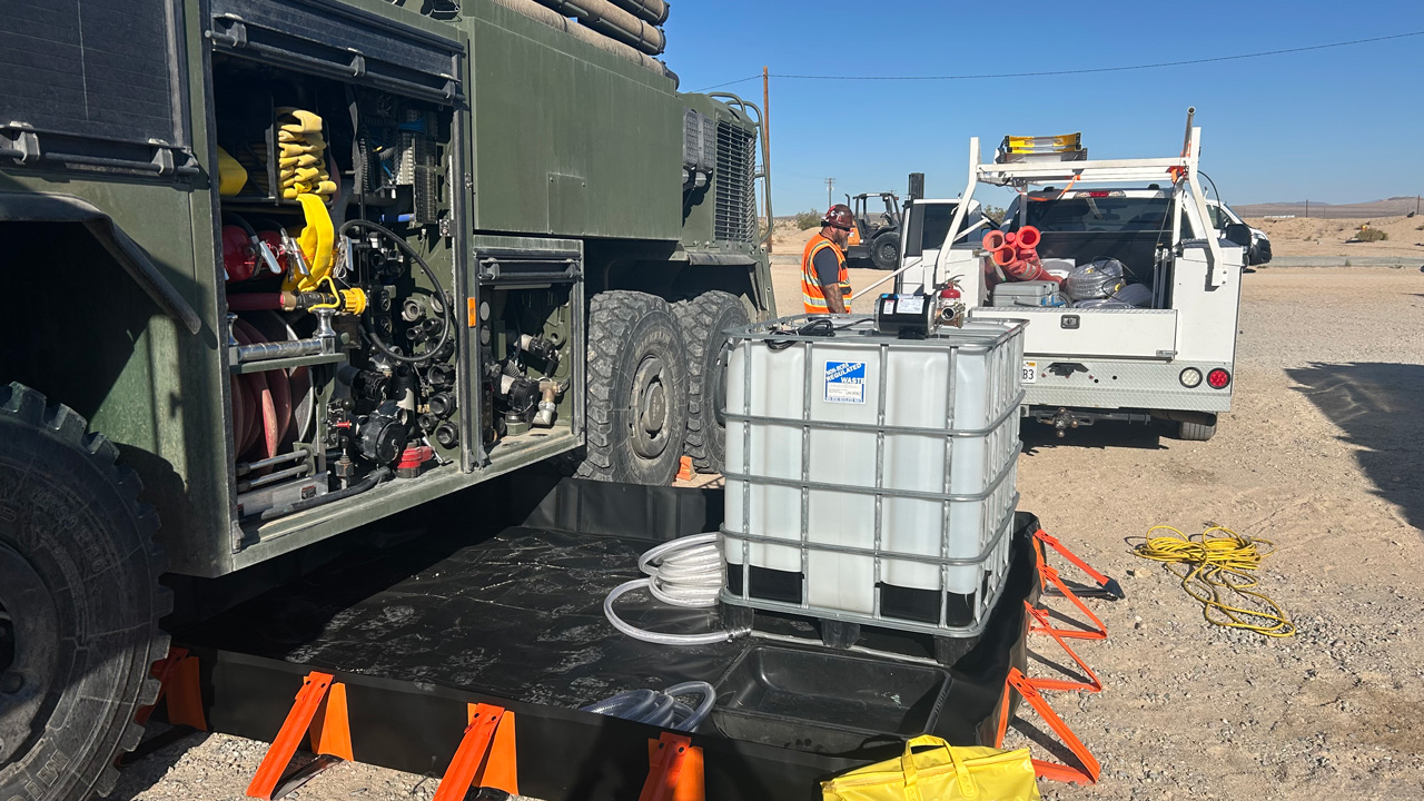 Field setup with a vehicle and water containment tank, hoses, and equipment in a desert environment