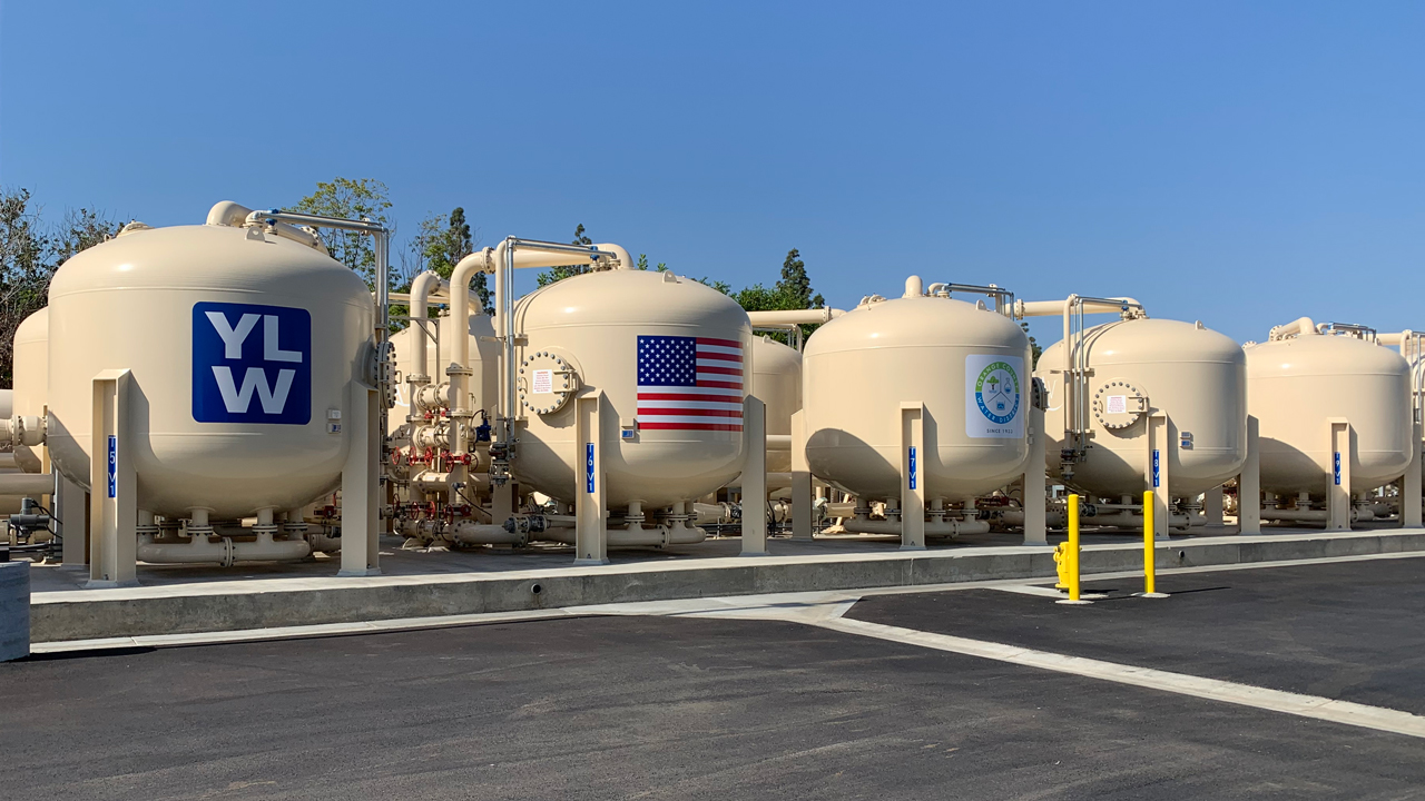 Large beige industrial tanks lined up outdoors under a clear blue sky