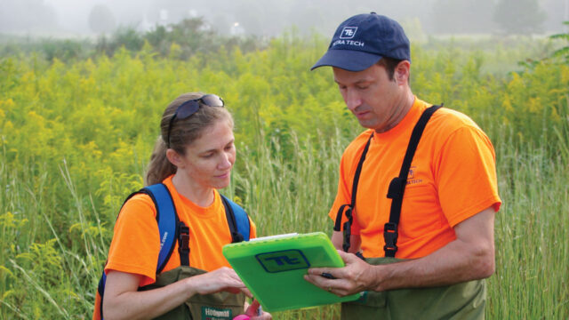 Two people looking at a clipboard in a grassland landscape