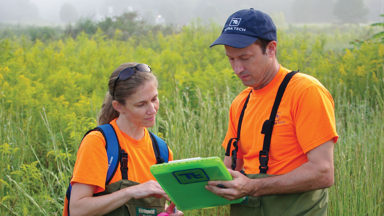 Two people looking at a clipboard in a grassland landscape