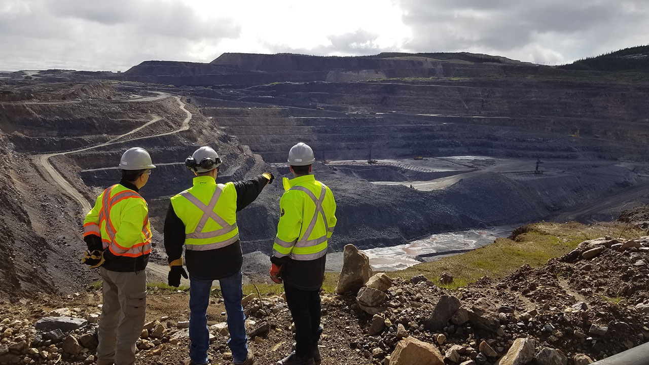 Three engineers survey a mine in a landscape