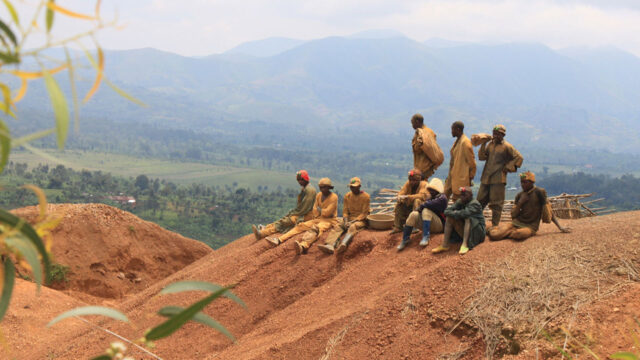 A group of artisanal miners sit on a hillside landscape