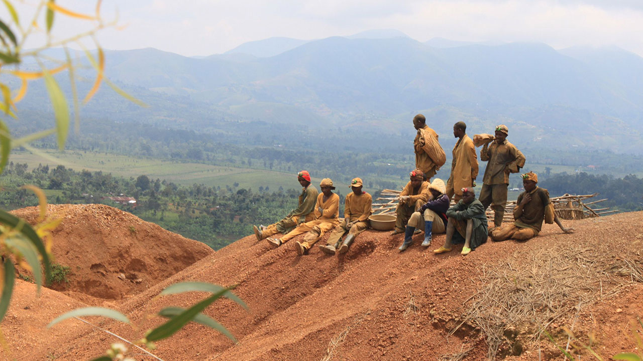 A group of artisanal miners sit on a hillside landscape
