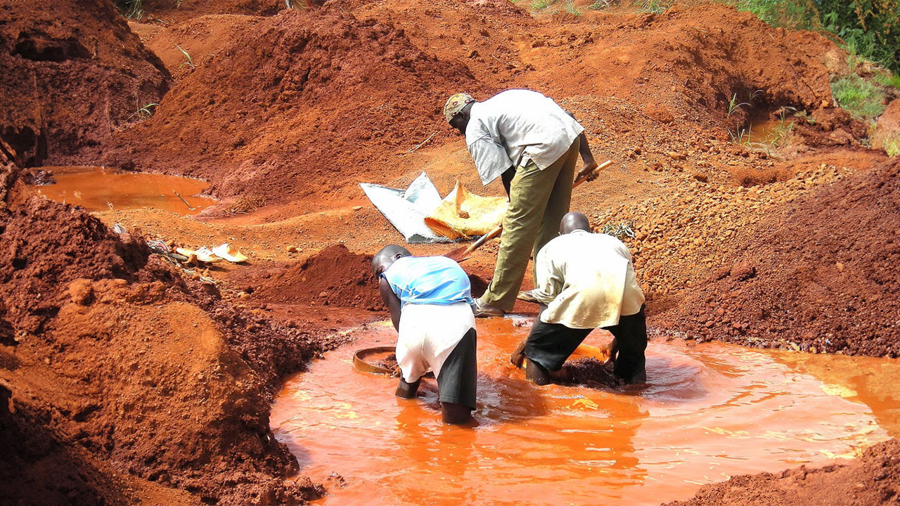 Three artisanal miners panning silt in a pool
