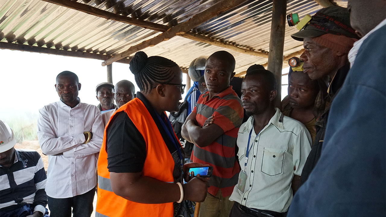 A person in a high visibility jacket talks to a group of local people