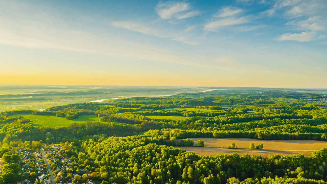 Aerial view of a forest, fields, and a river in the distance with a blue sky