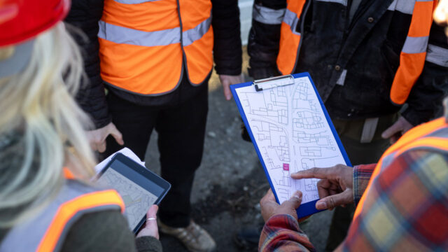 group of site workers review schematic design on clipboard and on a tablet